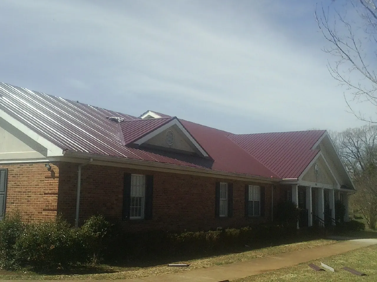 Red metal roof with gabled entries on a long brick building, from a Hail Damage Roof Repair job in Martinez